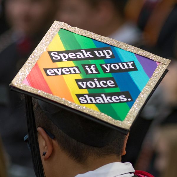 A young man wears a mortar board that reads "Speak up even if your voice shakes."