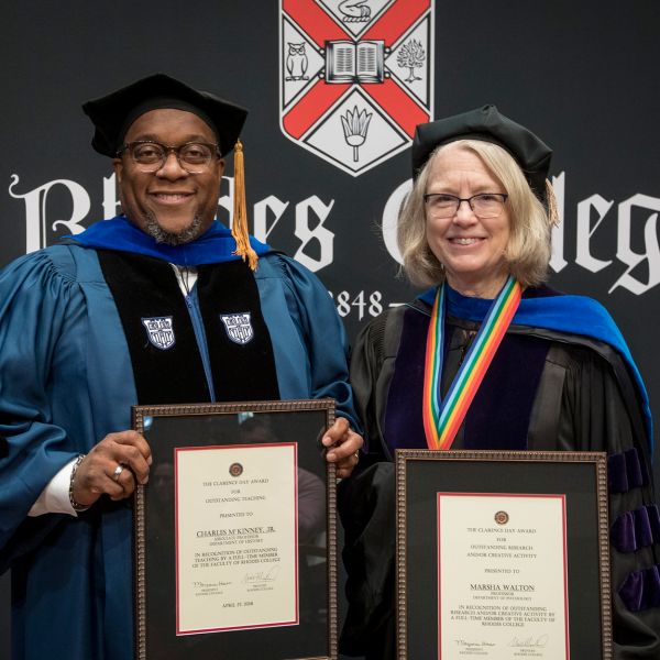 Two professors in regalia stand side by side with their distinguished awards.