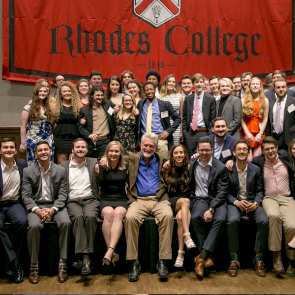 A group of alumni seated in rows in front of a Rhodes College banner.