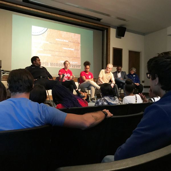 A group of professors, students, and activists sit in a panel discussion in front of an audience in a small lecture hall.