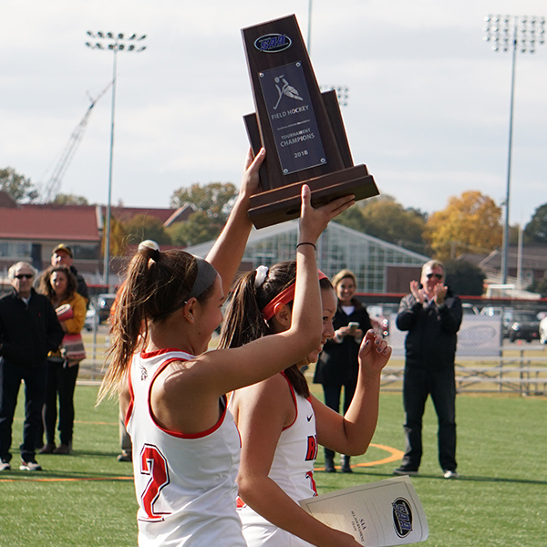 a female field hockey player holds up a trophy