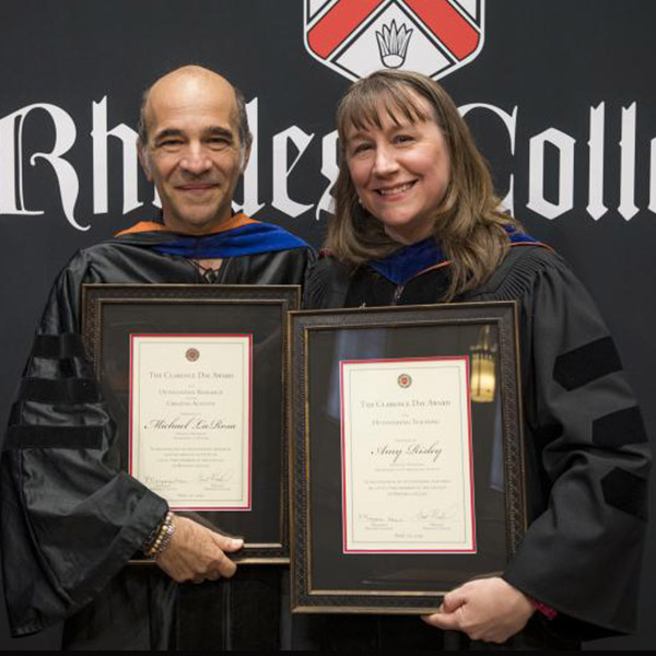 a male and female professor in academic robes, holding awards