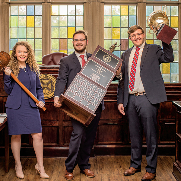 three students hold up mock trial trophies