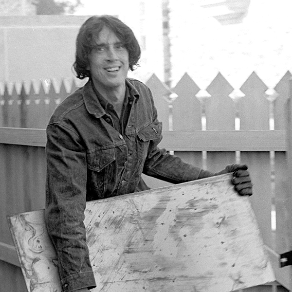 a man with dark hair holds a large stone slab and smiles at the camera