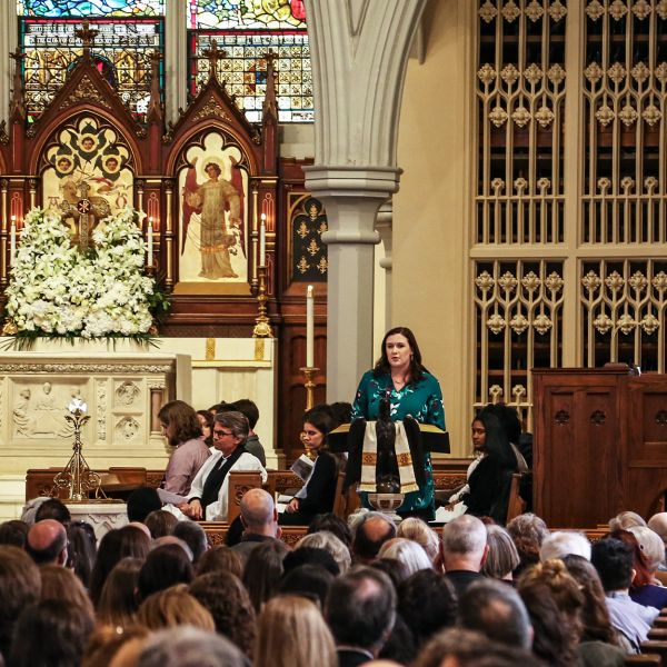 A woman in a green dress stands at a lectern in a crowded Episcopal church.