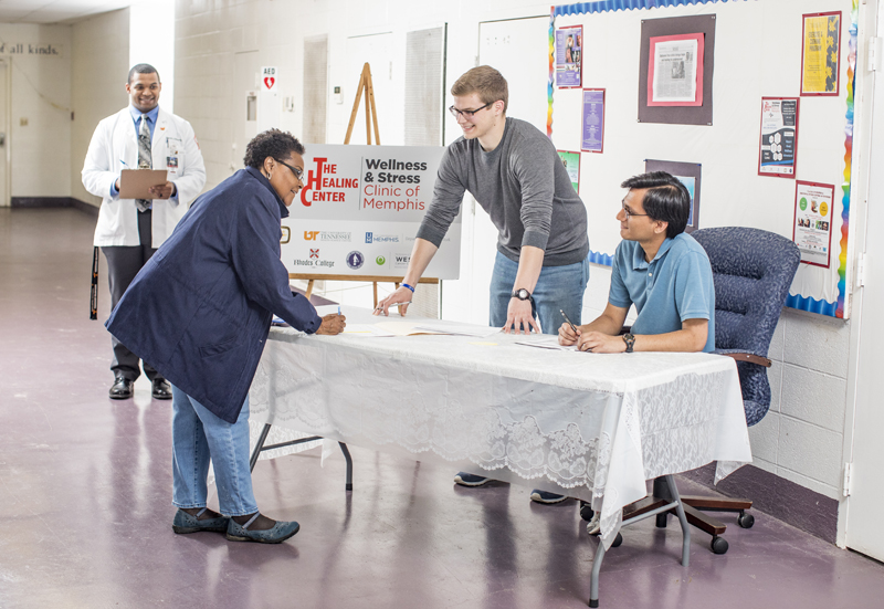 two male students help a patient sign in at the clinic