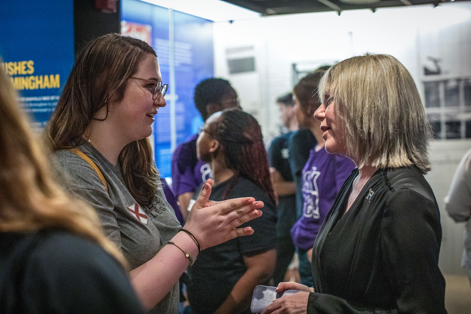 A gray-haired woman and a young student interact in a museum 