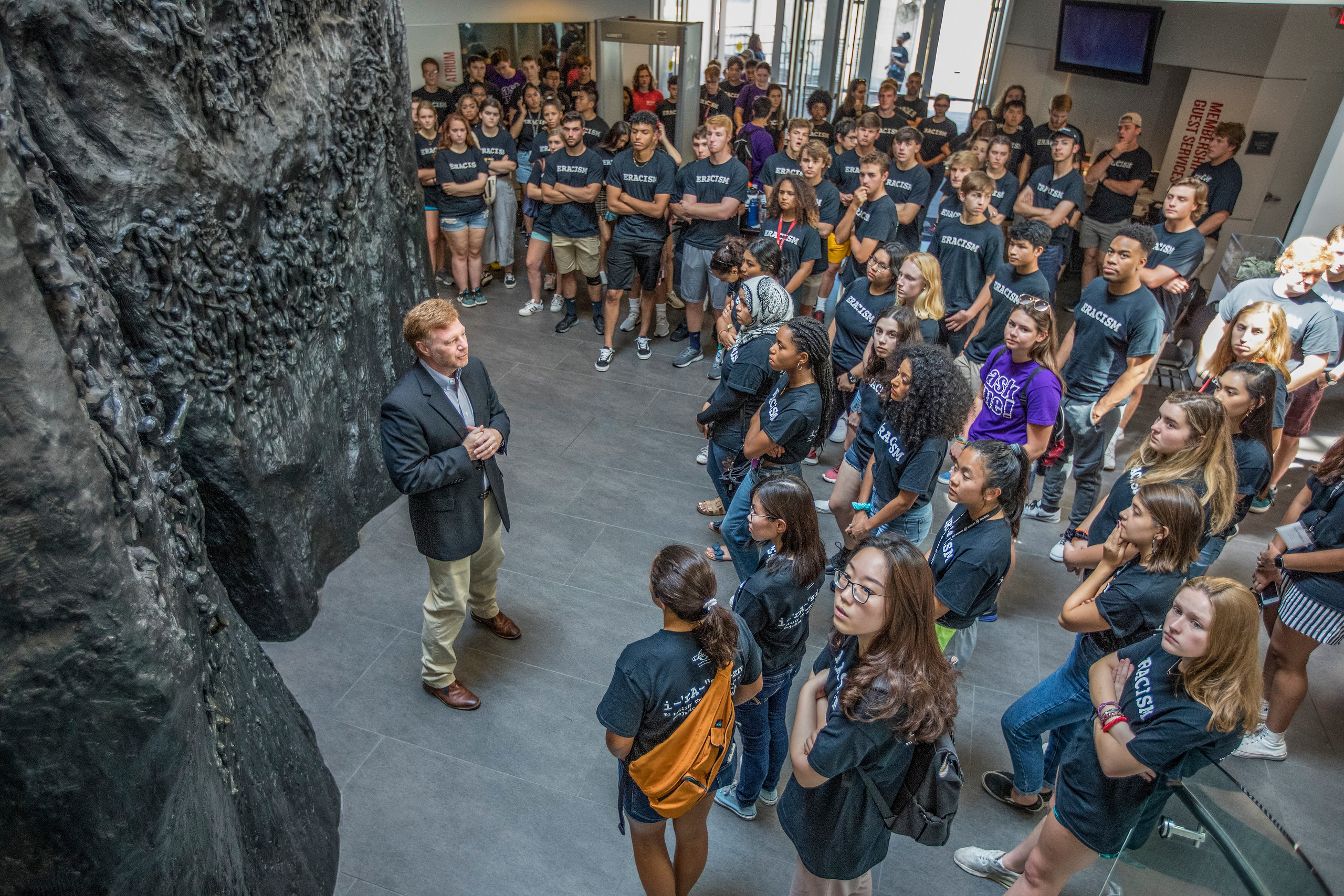 Students in matching shirts face red-haired man in suit