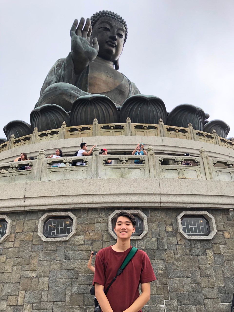 A young Asian male stands in front of a large statue of Buddha