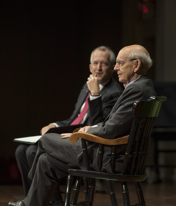 two men sit in chairs on a stage