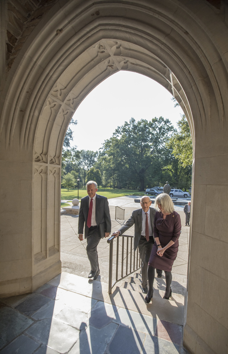 two men and a woman walk up steps through an arched doorway