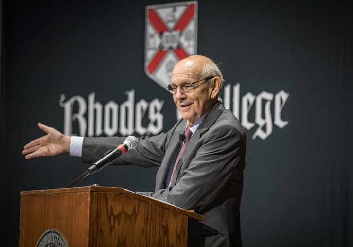 an older man stands at a podium and gestures toward the crowd