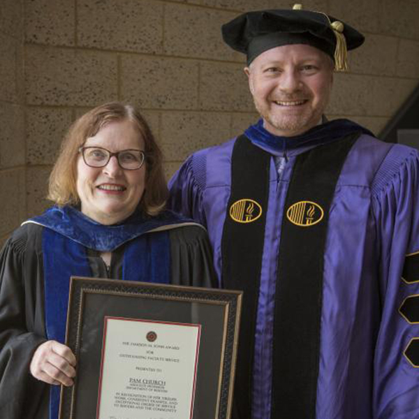 a man and a woman in academic robes smile at the camera