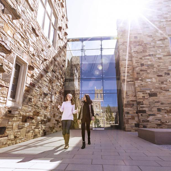 two female students walk out of glass and stone building