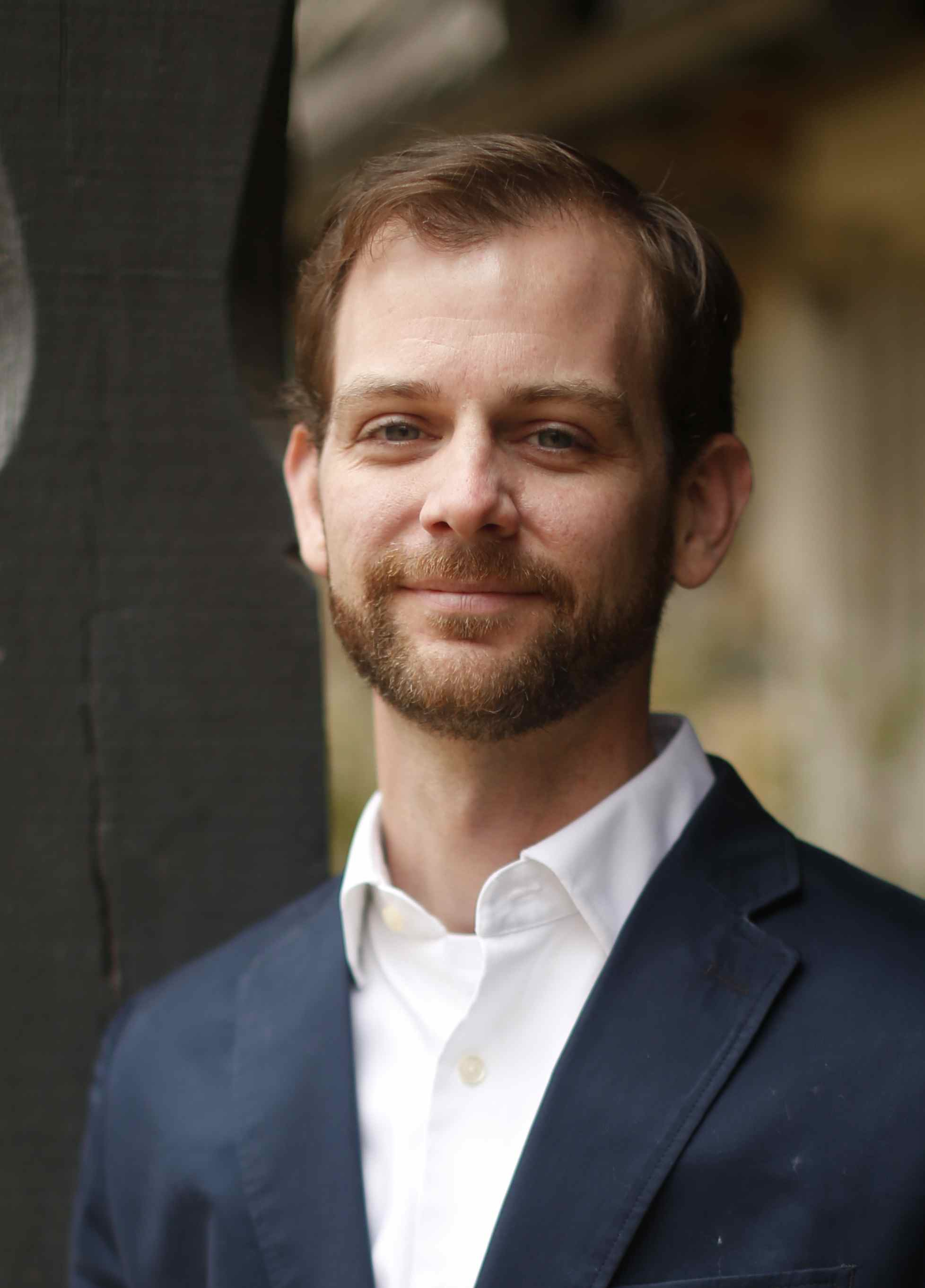 A bearded professor in an open collared white shirt and jacket.