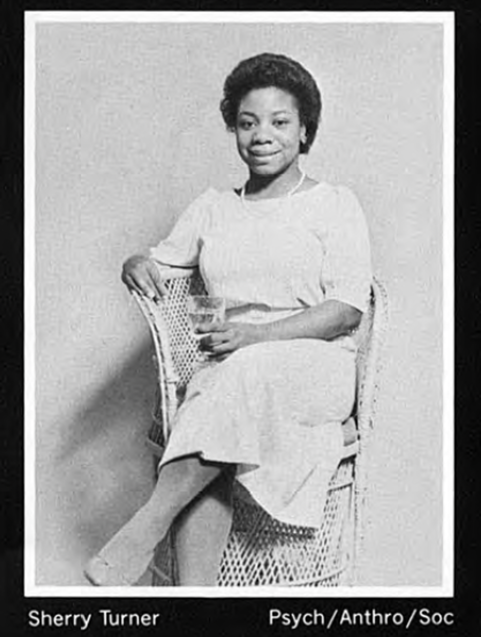 A young woman sits in a chair, holding a drink; photo in black and white 