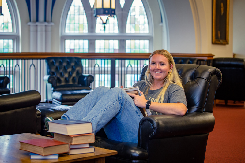 a young woman sits in a chair in a Gothic library