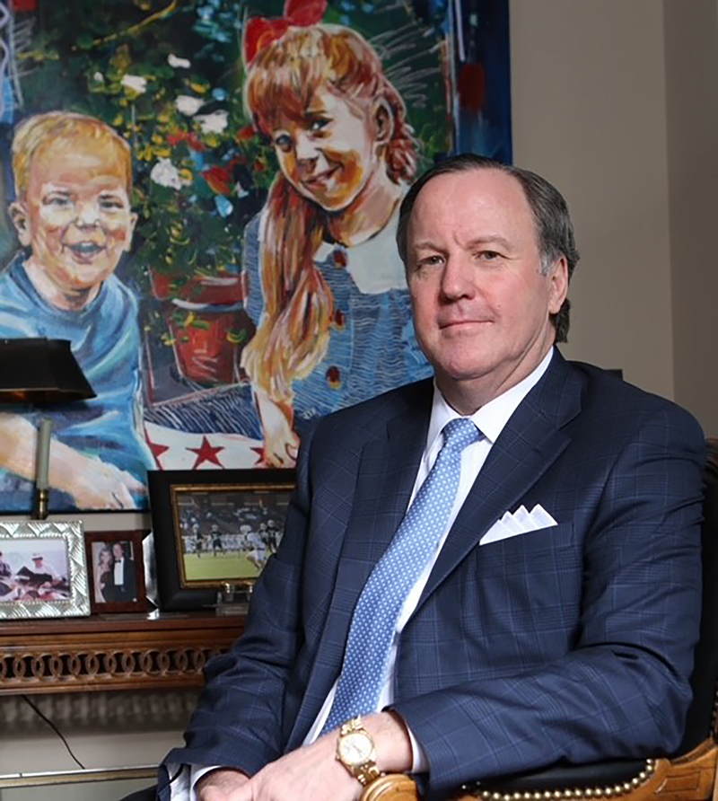 a man in a suit sits in front of a portrait of two children