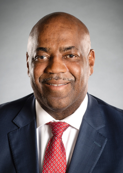 an African American man in a suit and tie smiles at the camers