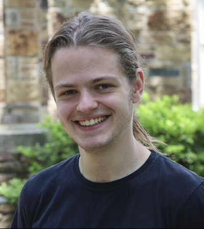 a young man with hair pulled back smiles at the camera