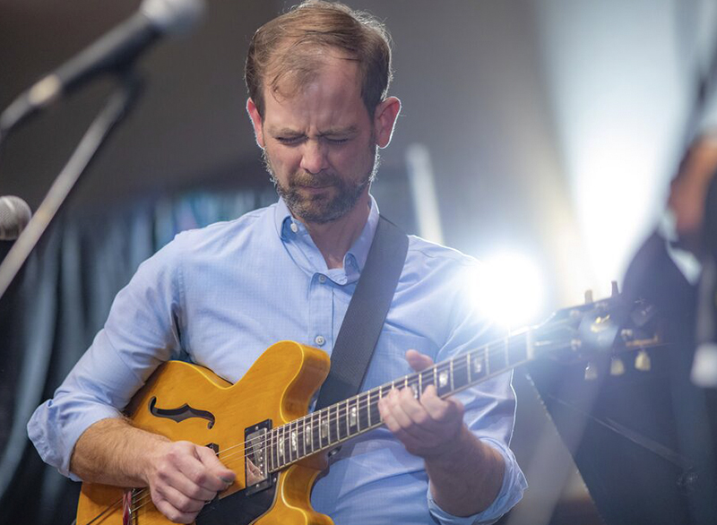 John Bass playing the guitar on stage