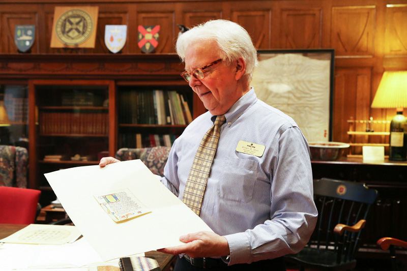  white-haired man holds a page from an illustrated manuscript