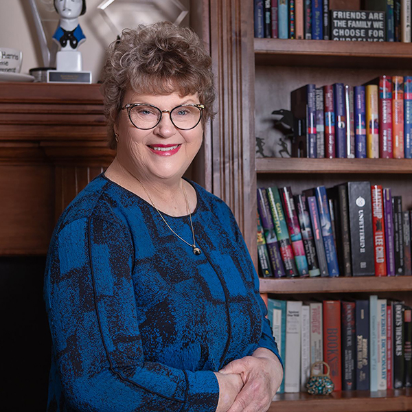 a woman in glasses stands next to a bookshelf