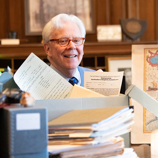 a white-haired gentleman surrounded by piles of documents
