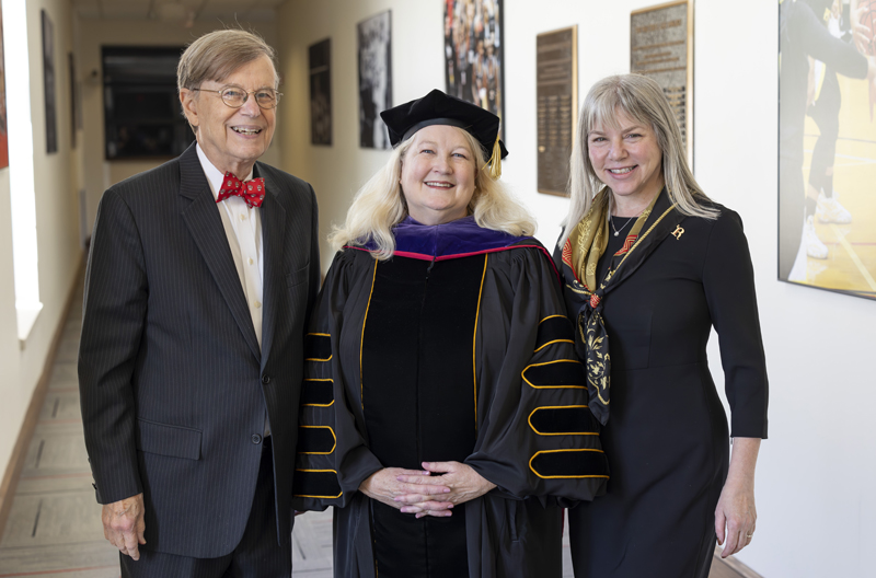 a woman in academic robes flanked by a man and woman
