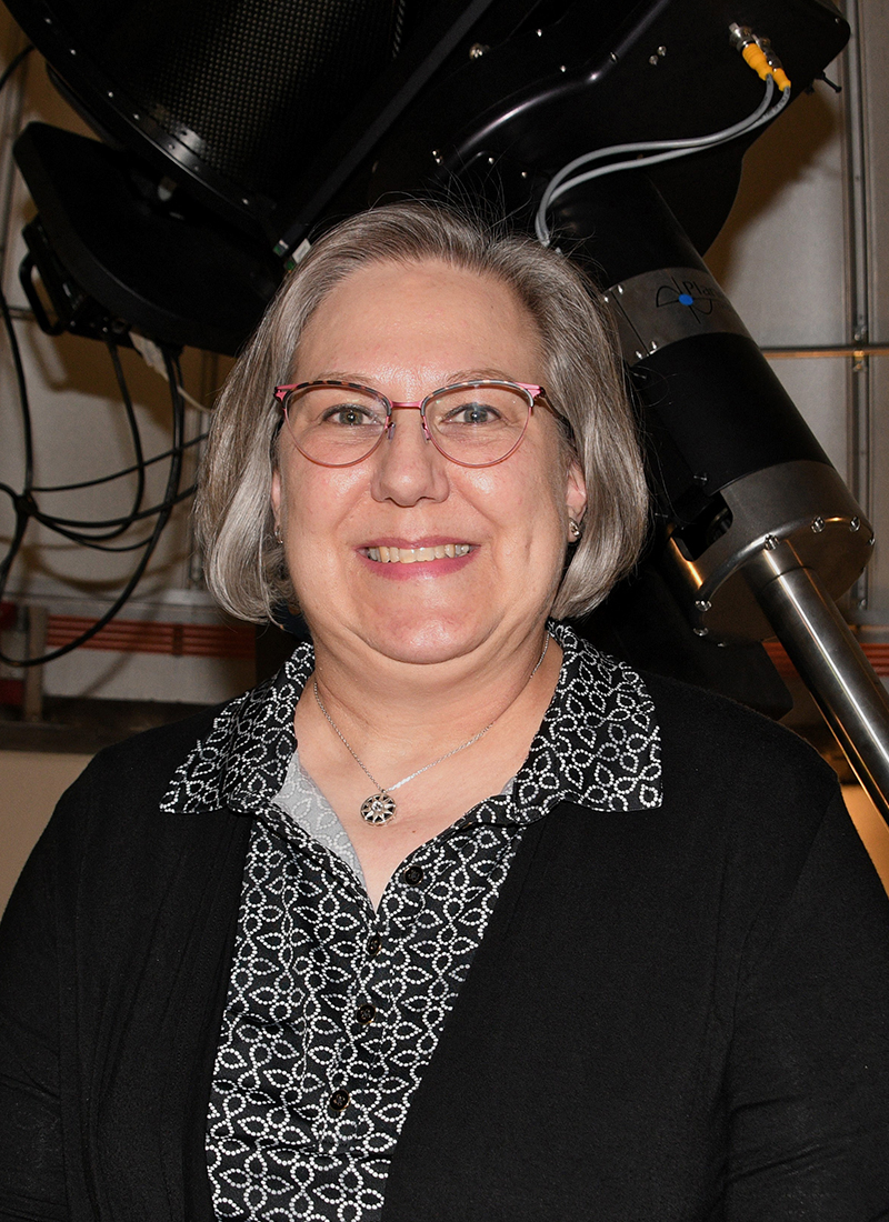 a woman poses in front of a large telescope