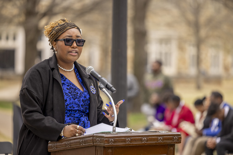 a young African American woman speaks at an outdoor lectern