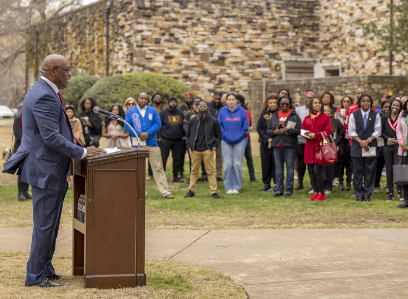 an African American man speaks at an outdoor lectern