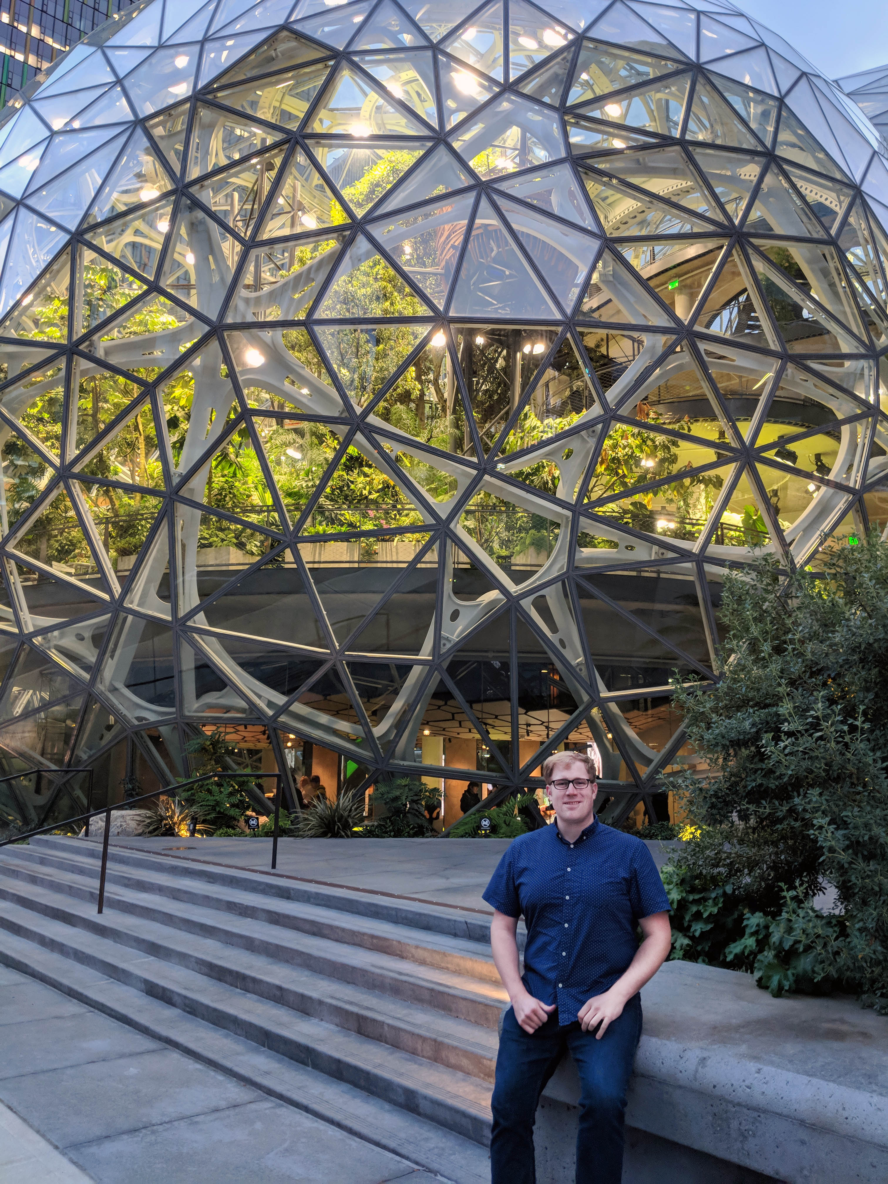 A man sits on steps in front of spherical glass and metals architecture on Amazon's campus