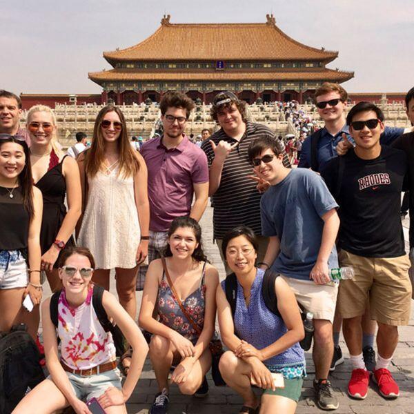 A group of casually dressed students and their professors stand together in front of 