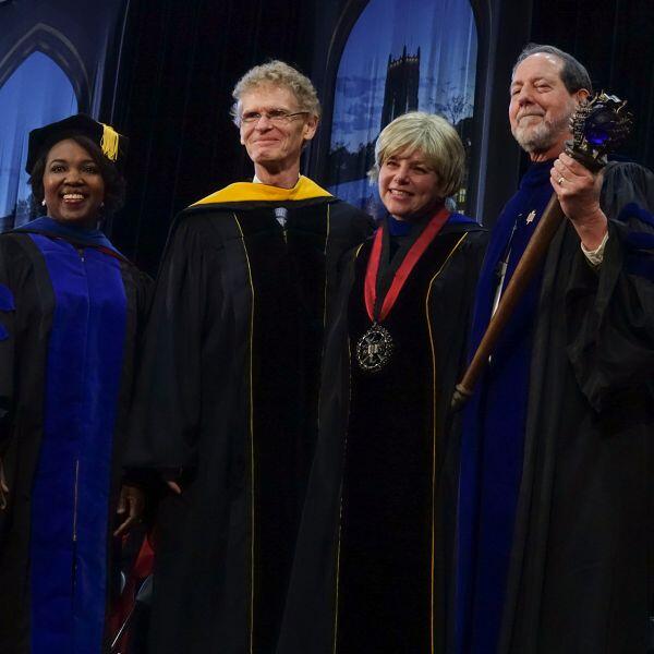 A group of professors gather around a woman in presidential regalia.