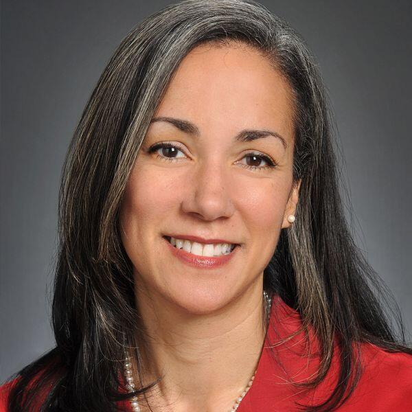 A dark haired woman woman in a red blazer smiles warmly.