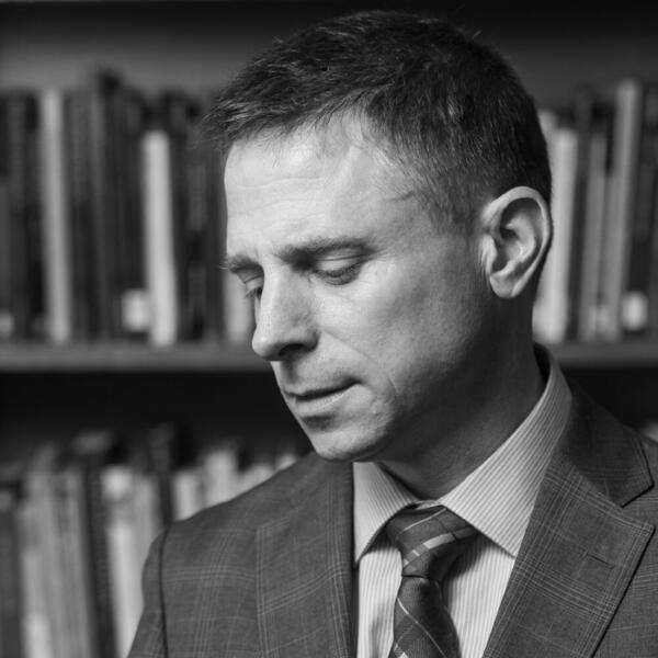 A black and white photo of a professor in suit and tie standing in is library.