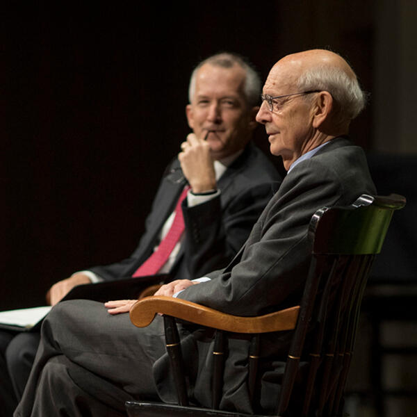 two men sit in chairs on a stage