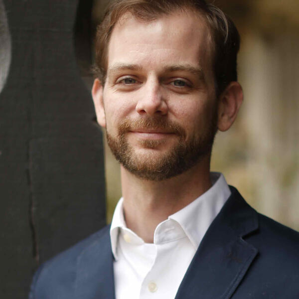 A bearded professor in an open collared white shirt and jacket.