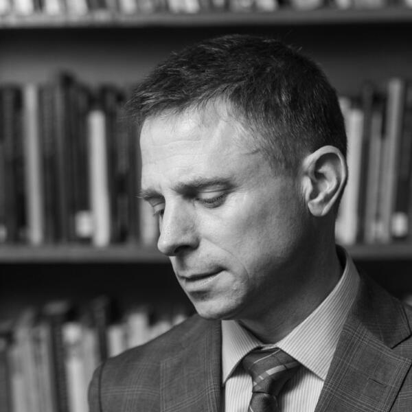 A professor, seen in black and white, stands before his bookshelf.