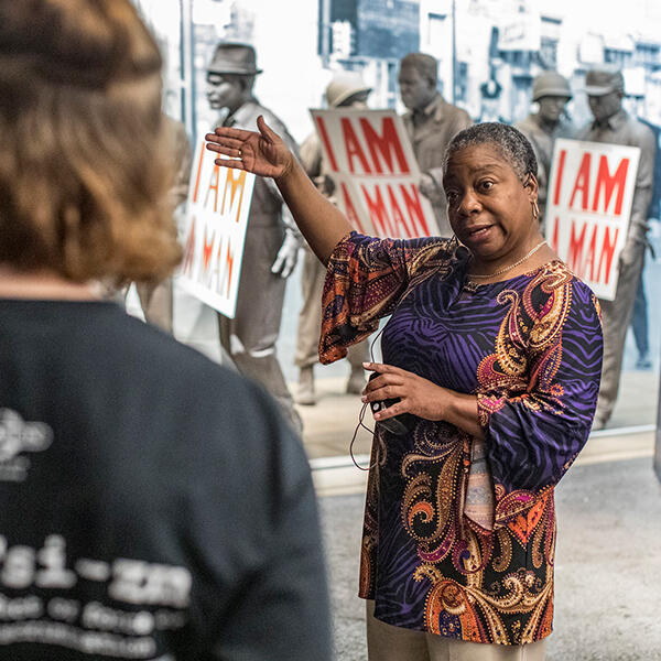 an African American woman gestures while talking to students