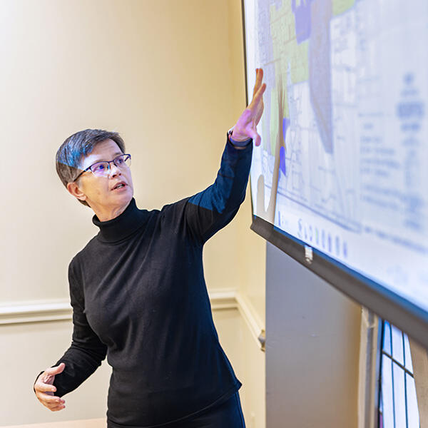 a woman lectures while pointing to a screen