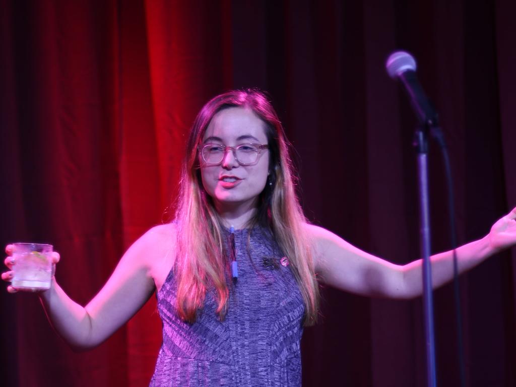 A woman stands in front of a red curtain and in front of a mic