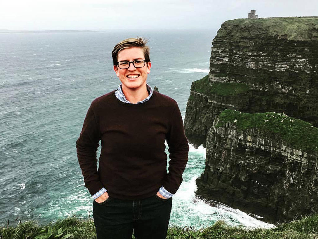 A woman with short hair stands on a cliff in front of the sea