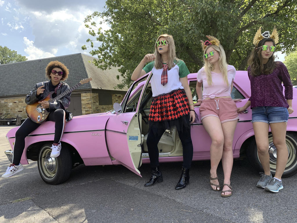 Four students dressed in costumes lean against a vintage car