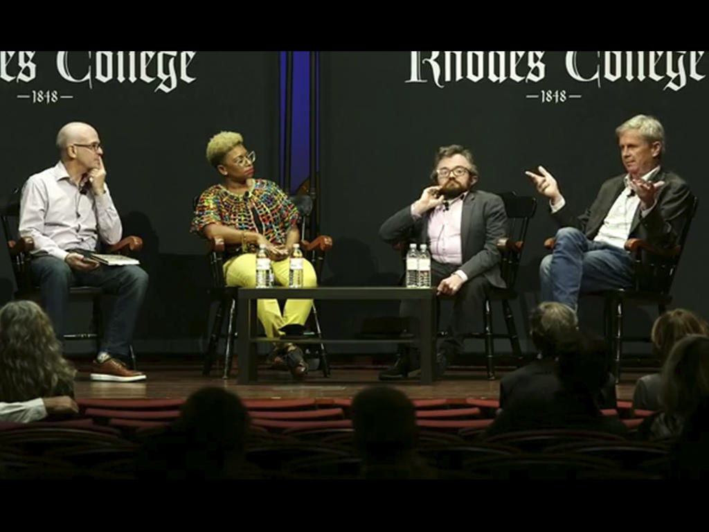 three men and a woman seated in chairs on a stage