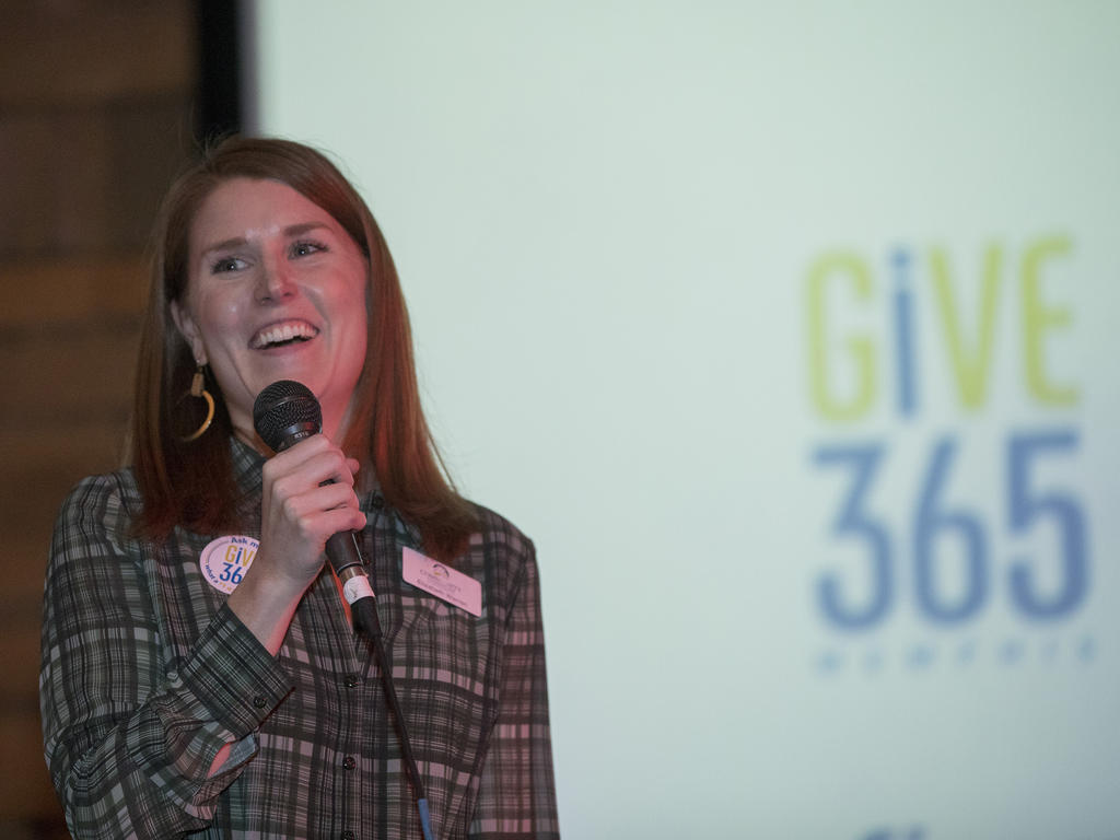 a young woman speaking on a microphone in front of a Give365 backdroop