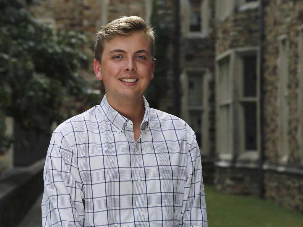 A blonde man stands in front of neogothic stone building