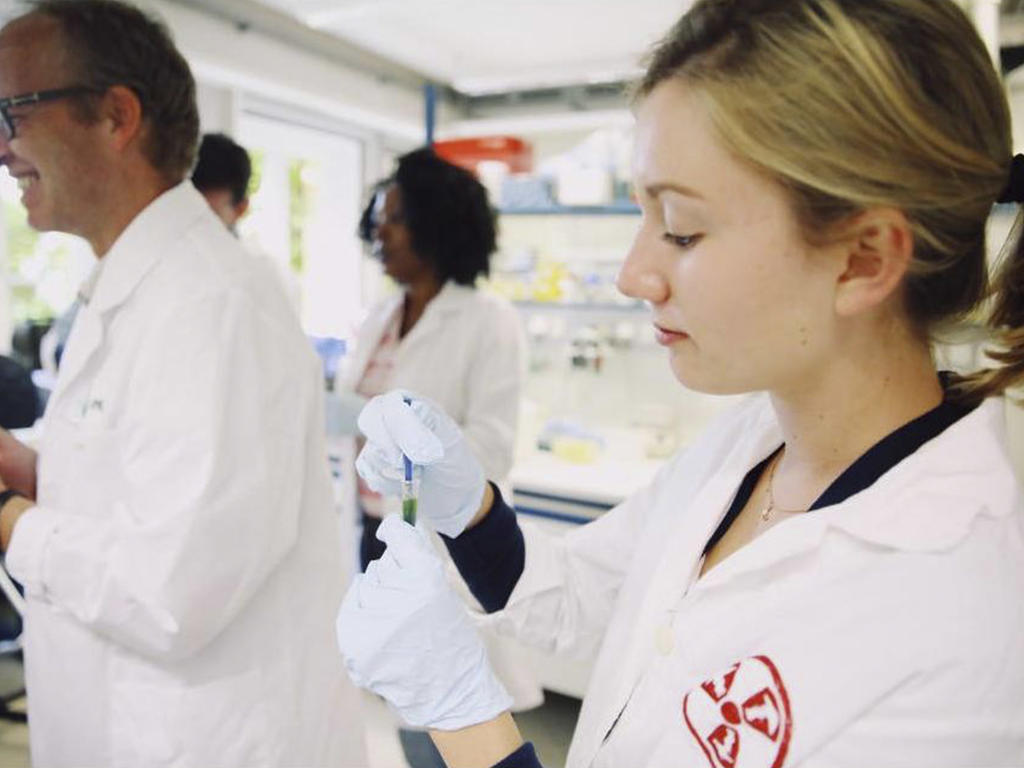 a female in a lab coat tests a liguid in a test tube