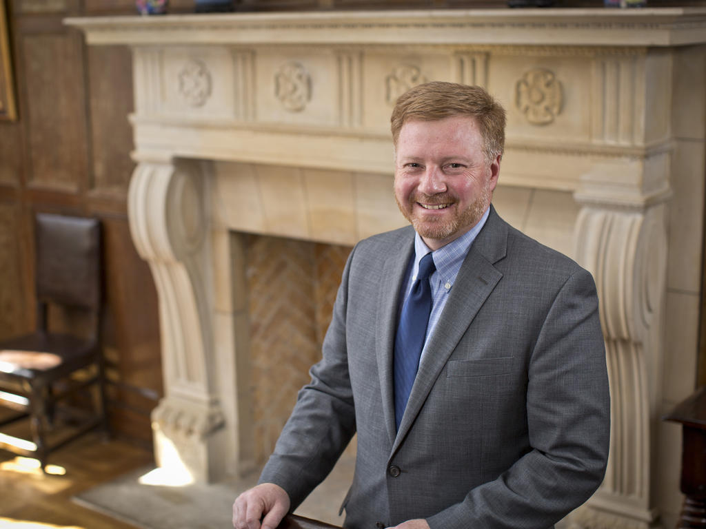 Man in front of fireplace with hands on chair